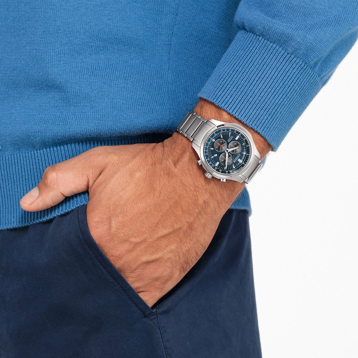 Mann mit Uhr, blauem Pullover und marineblauer Hose, Hand in der Tasche.