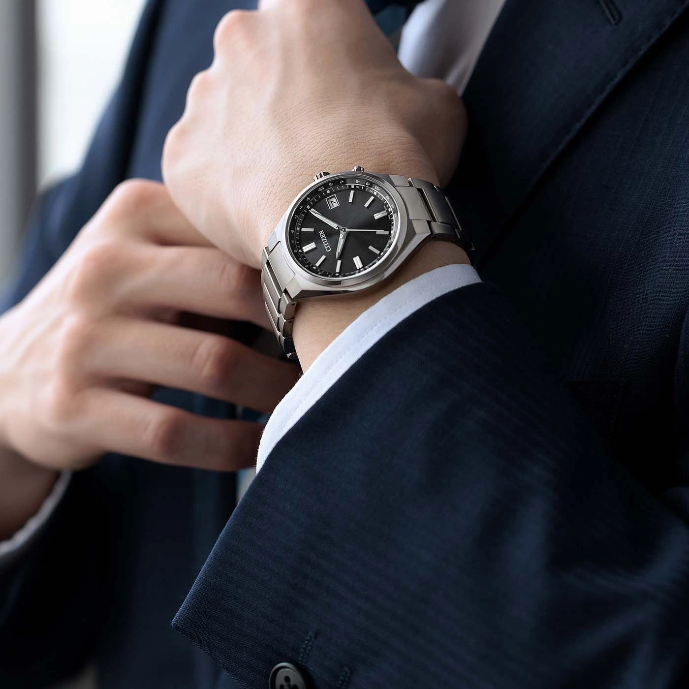 Mann im Anzug richtet seine Krawatte, trägt eine Armbanduhr.
