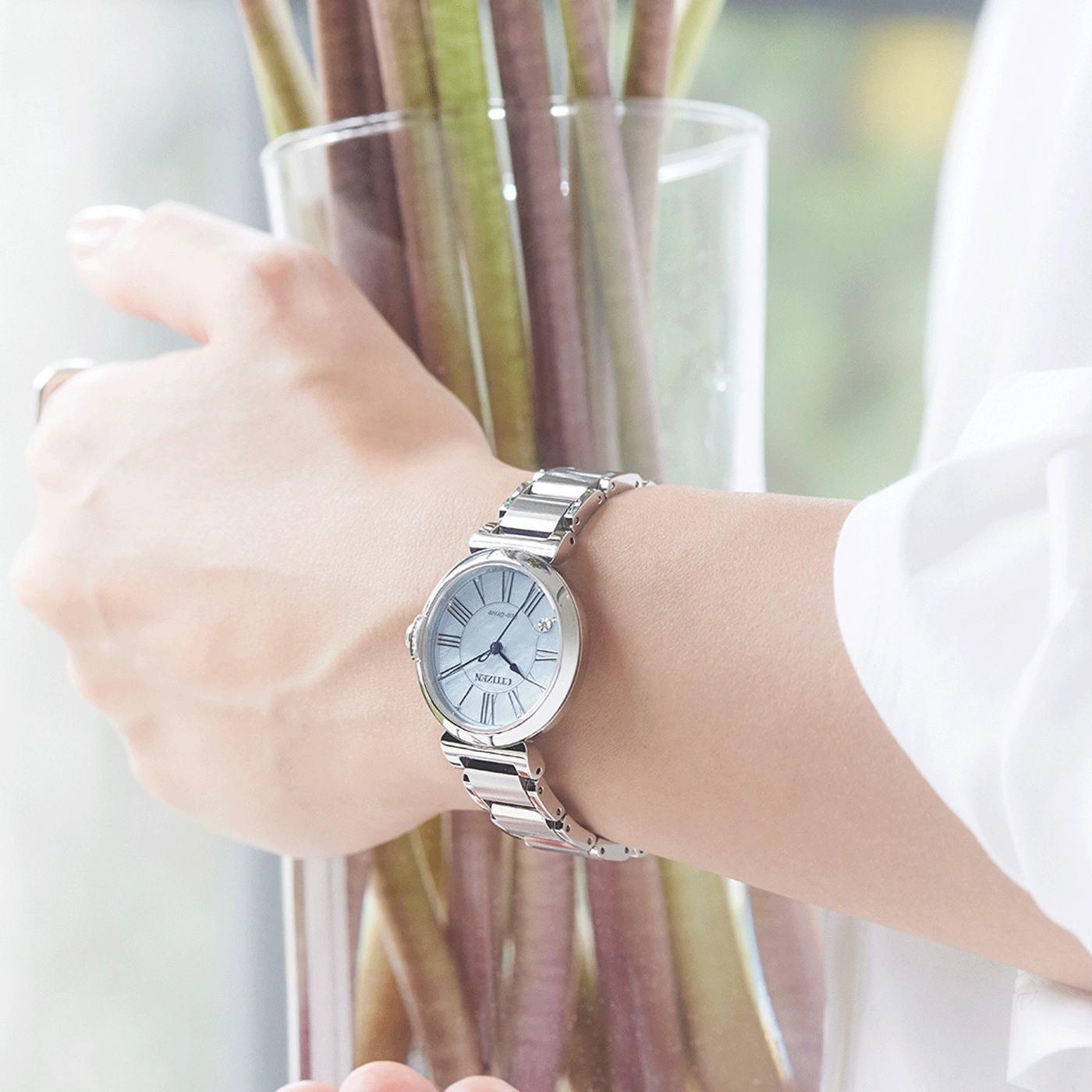 Ein silberne Uhr am Handgelenk einer Frau, die eine Vase mit Pflanzen hält.