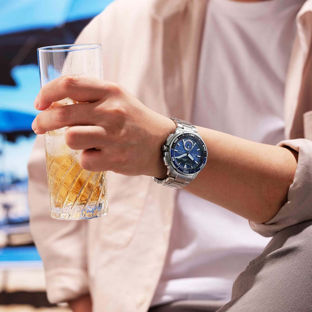 Eine Person hält ein Glas mit eisigem Getränk und trägt eine silberne Uhr.