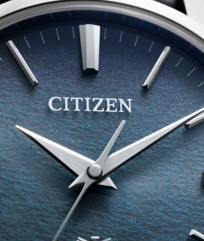 Nahaufnahme eines Citizen-Zifferblatts mit silbernen Zeigern und Markierungen auf einem blauen, strukturierten Zifferblatt.