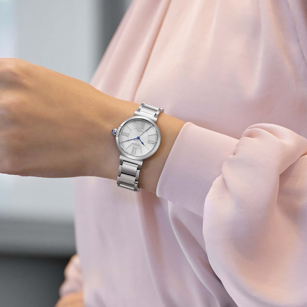 Das Handgelenk einer Frau mit einer silbernen Uhr mit weißem Zifferblatt und römischen Ziffern.