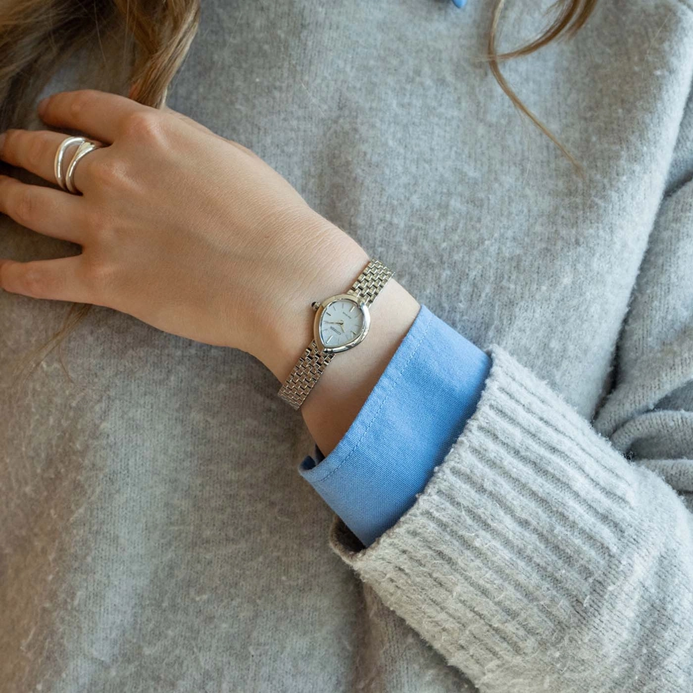 Frau mit Pullover, Hemd, Uhr und Ring.