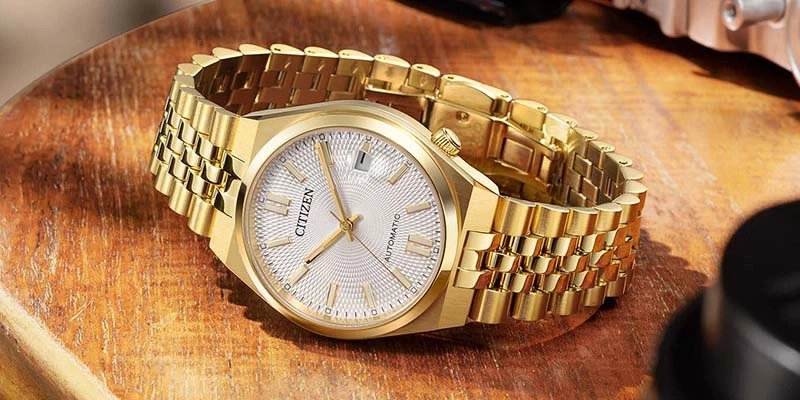 Eine goldene Citizen Automatik-Uhr mit strukturiertem Zifferblatt auf Holzoberfläche.