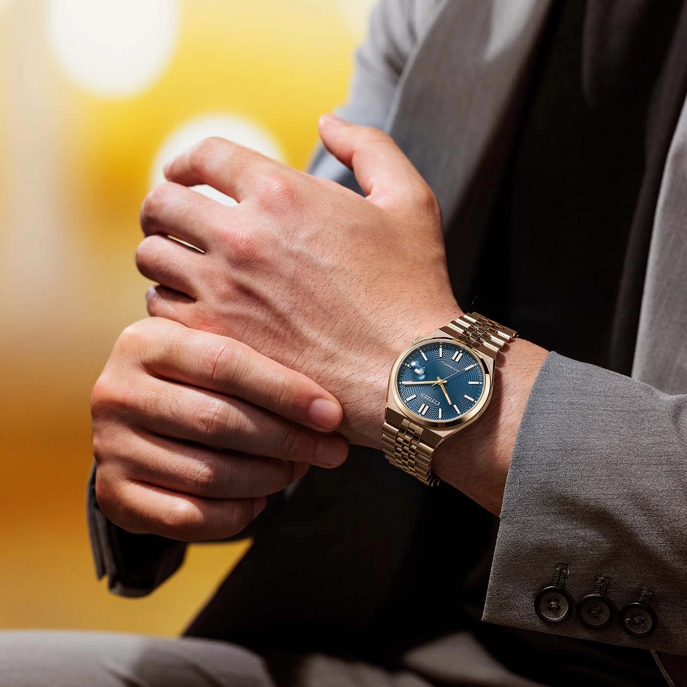 Mann trägt goldene Uhr mit blauem Zifferblatt und grauen Anzug.