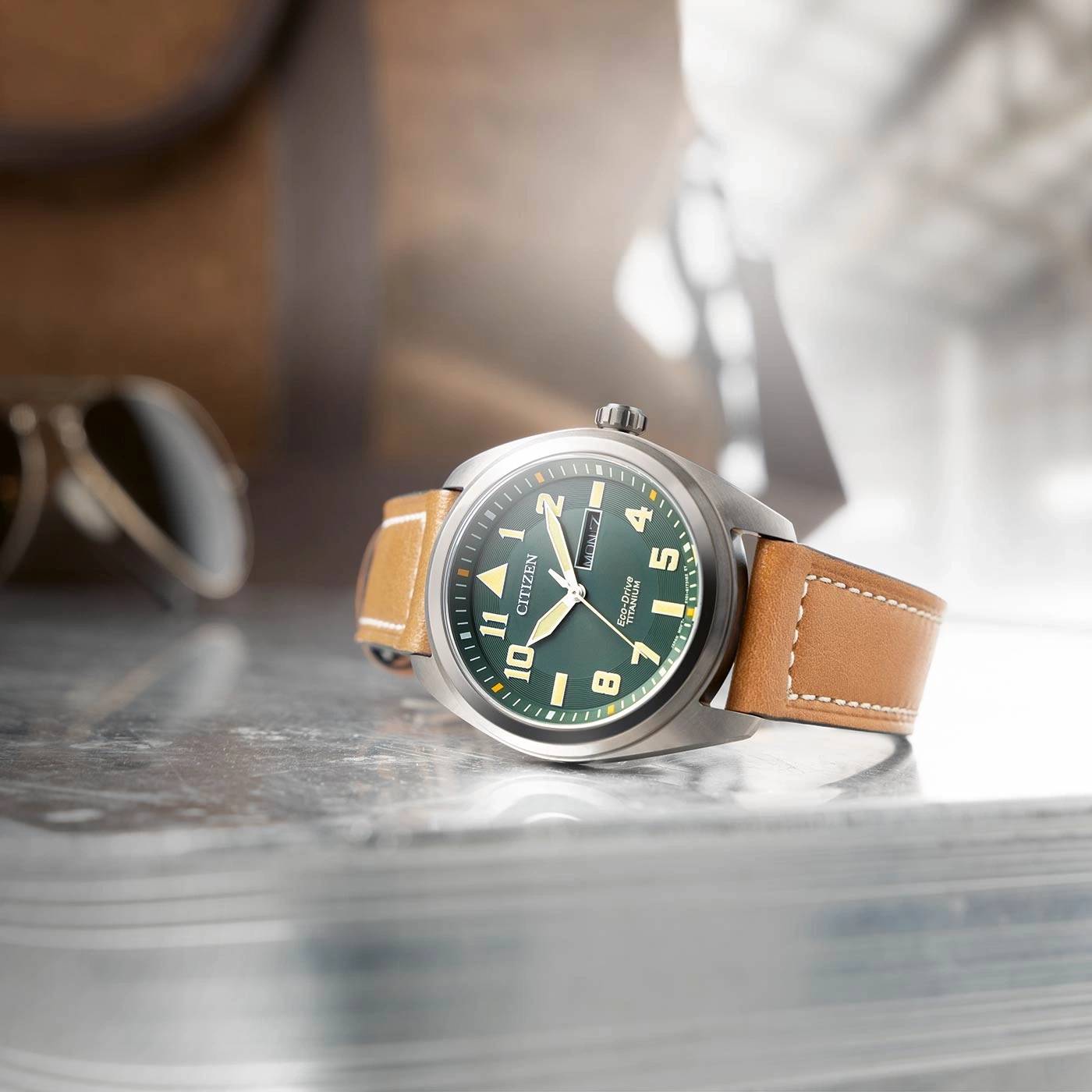 Citizen-Uhr mit grünem Zifferblatt und braunem Lederarmband auf reflektierender Oberfläche.