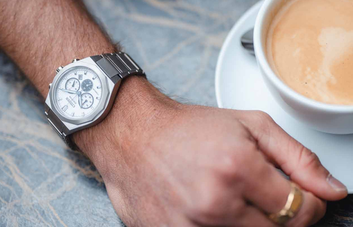 Mann mit Citizen-Uhr und einer Tasse Kaffee daneben