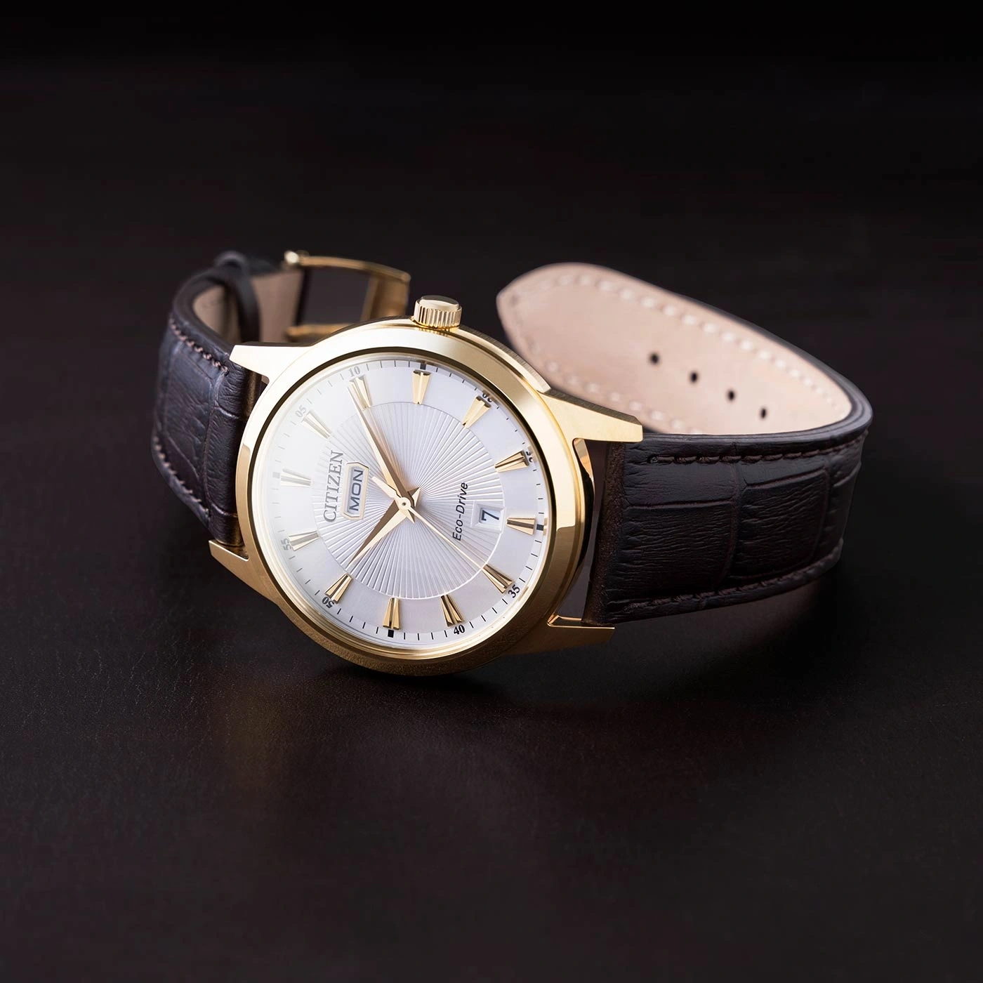 Goldene Citizen-Uhr mit Lederarmband auf dunkler Oberfläche.