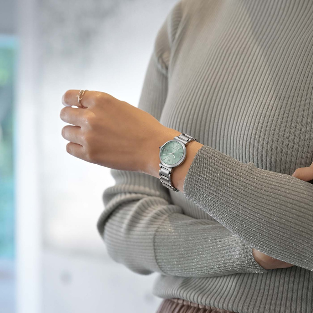 Eine Frau mit einer silbernen Uhr und einem grauen Pullover.