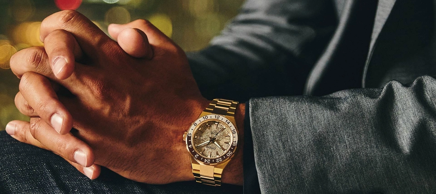 Mann mit goldener Uhr, Hände gefaltet, Anzugjacke, Bokeh-Hintergrund.