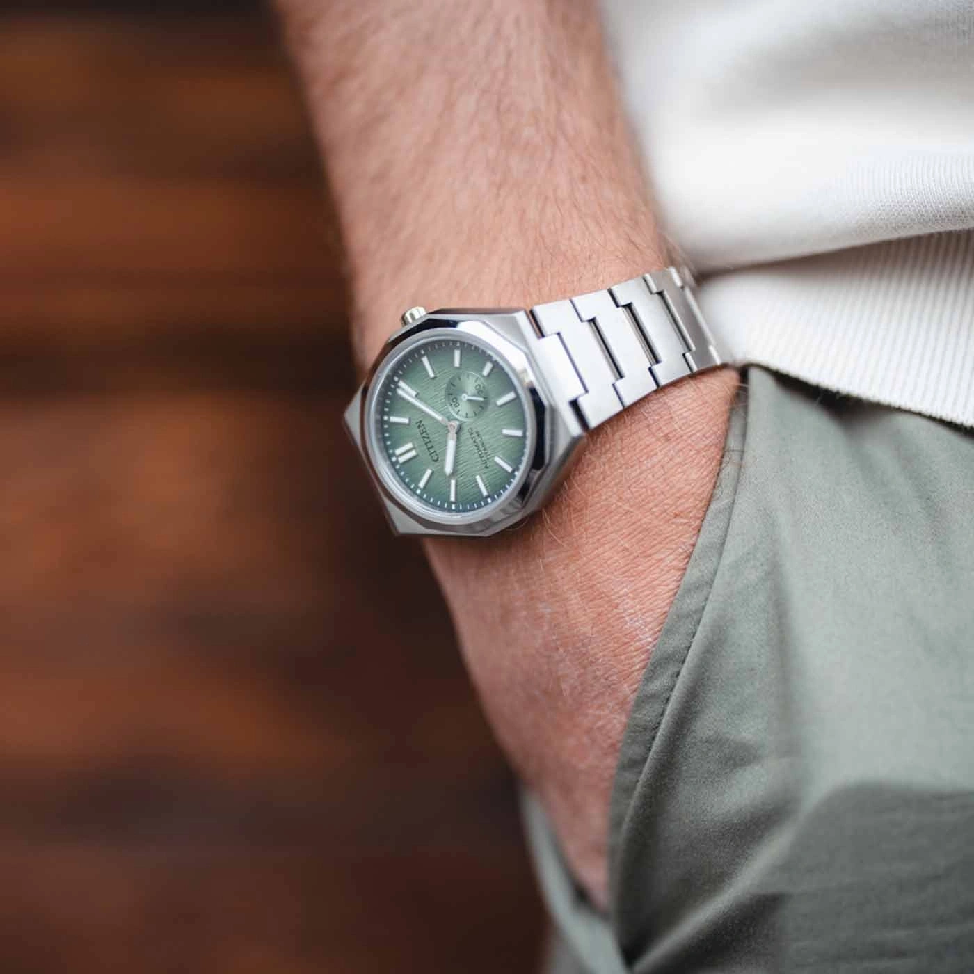 Eine Person trägt eine Citizen-Uhr mit grünem Zifferblatt und silbernem Armband.