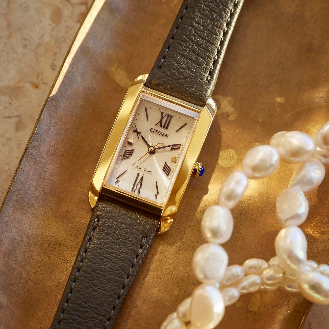 Citizen-Uhr mit goldenem Gehäuse und Lederarmband, neben Perlen.