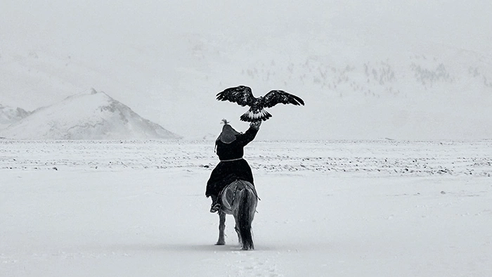 Ein Mann auf einem Pferd mit einem Adler in einer verschneiten Landschaft.