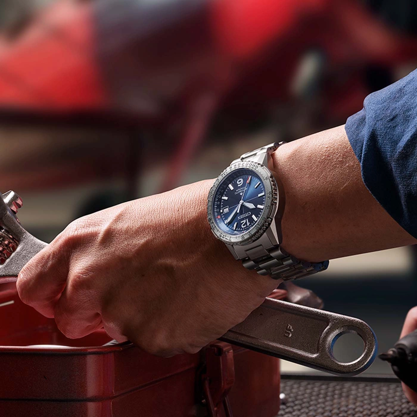 Nahaufnahme einer Person, die eine Uhr trägt und einen Schraubenschlüssel hält und an einem Auto arbeitet.