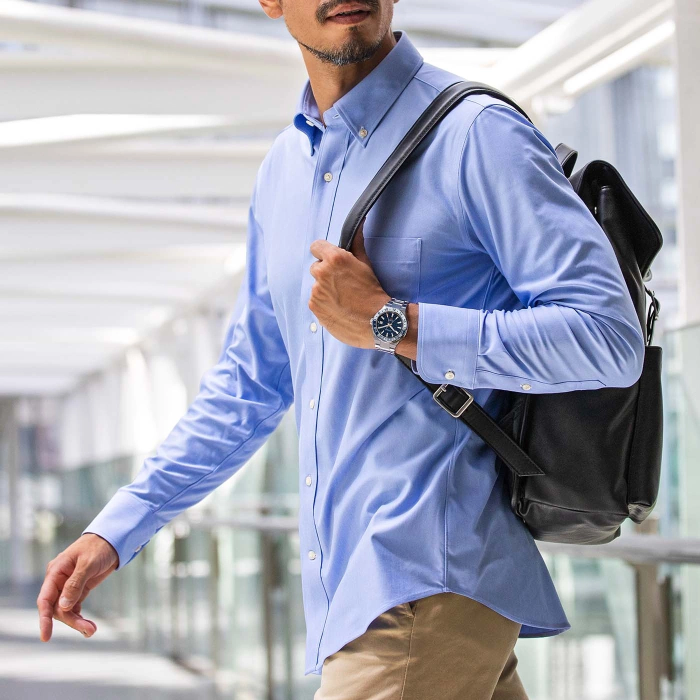 Mann im blauen Hemd mit Uhr und Rucksack geht in einem Gebäude