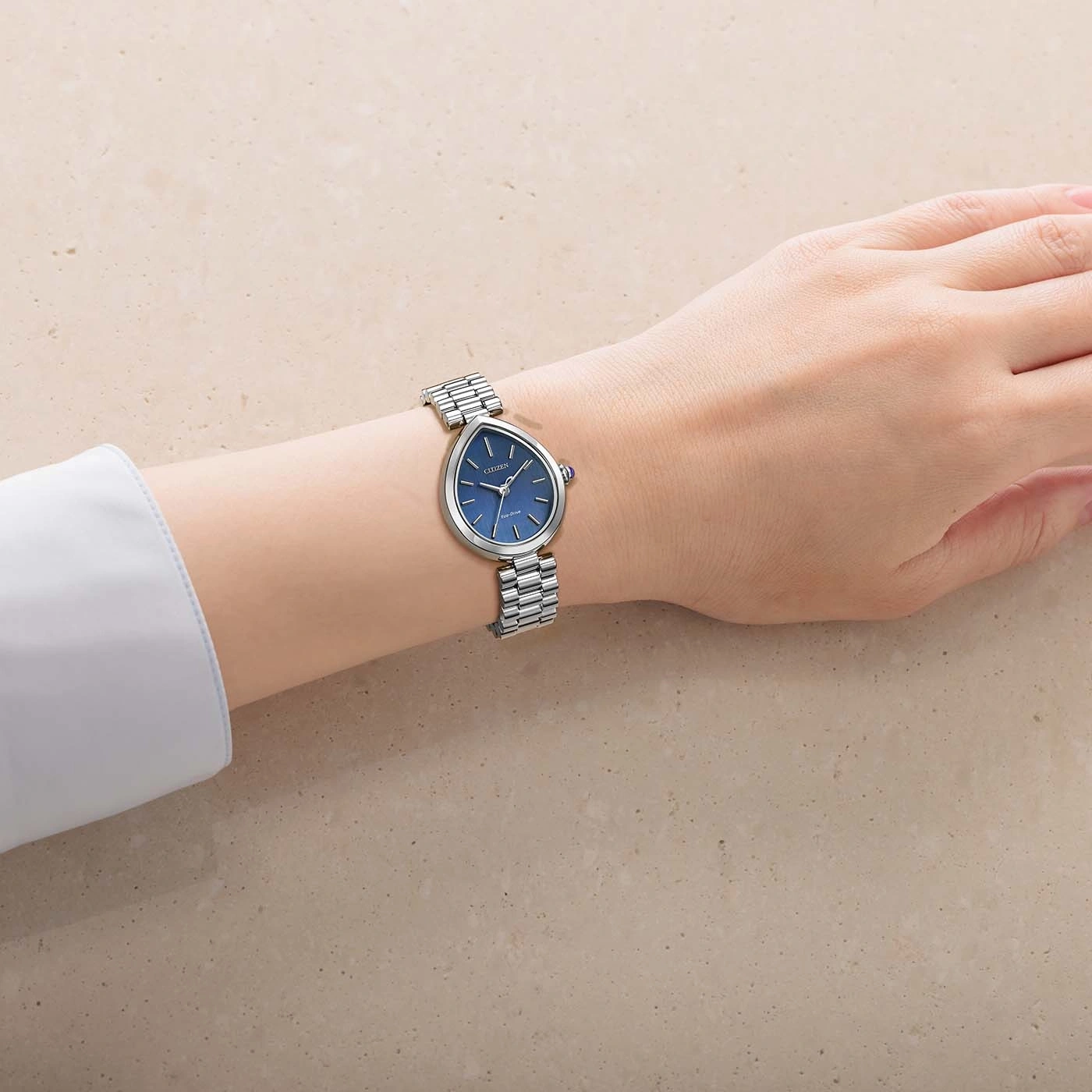 Das Handgelenk einer Frau trägt eine silberne Uhr mit blauem Zifferblatt.