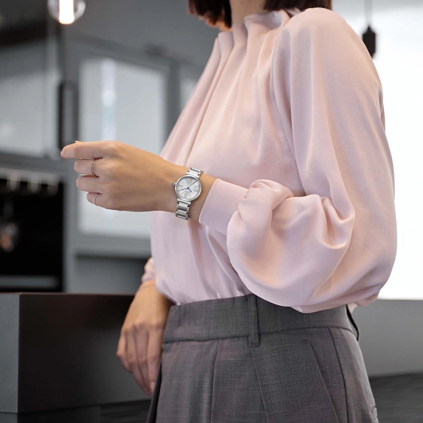 Frau in rosa Bluse und grauer Hose prüft ihre Uhr.