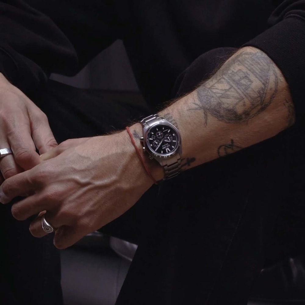 Nahaufnahme des tätowierten Arms eines Mannes mit Uhr und Ringen.