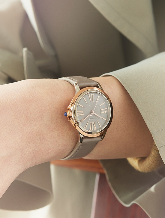Nahaufnahme einer Armbanduhr mit grauem Armband und goldenen Details am Handgelenk.
