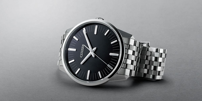 Citizen-Uhr mit schwarzem Zifferblatt und silbernem Armband auf grauem Untergrund