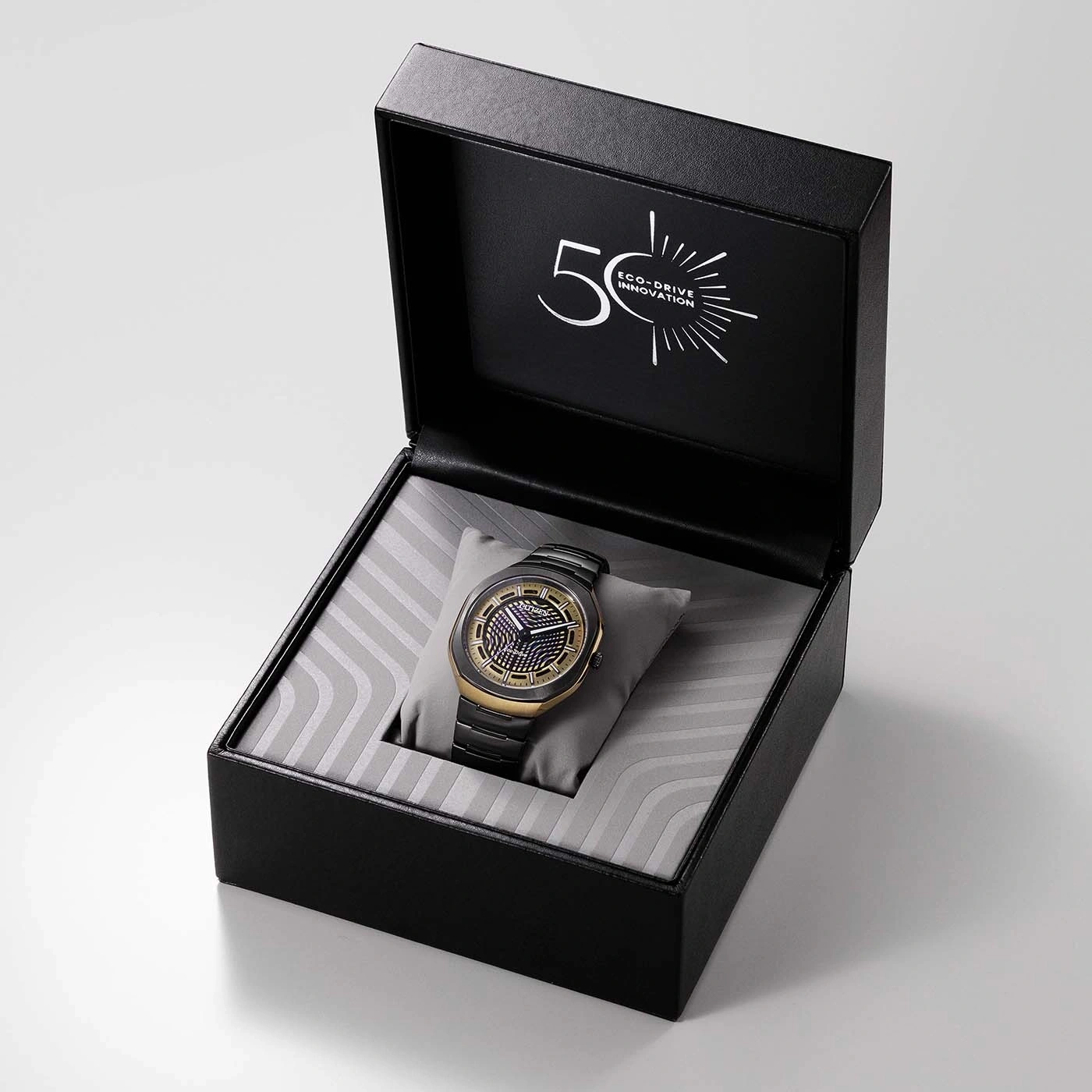 Eine schwarz-goldene Uhr in einer offenen Schachtel mit dem Aufdruck „50 ECO-DRIVE INNOVATION“ auf dem Deckel.