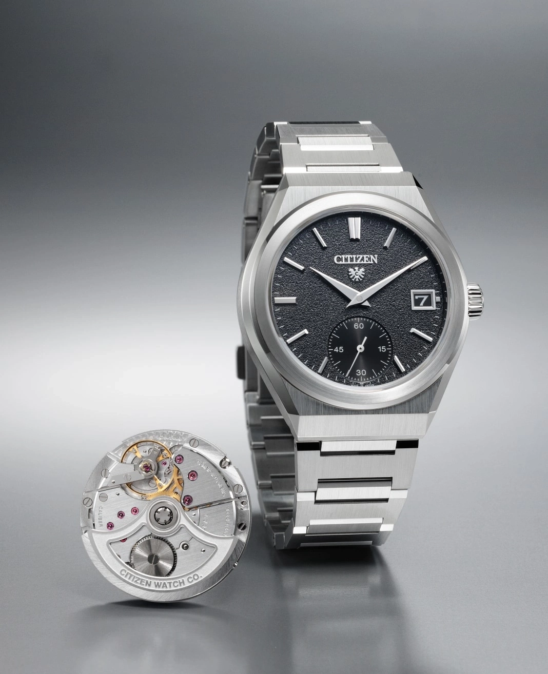 Citizen-Uhr mit freiliegendem Mechanismus und Edelstahlarmband auf grauem Untergrund.