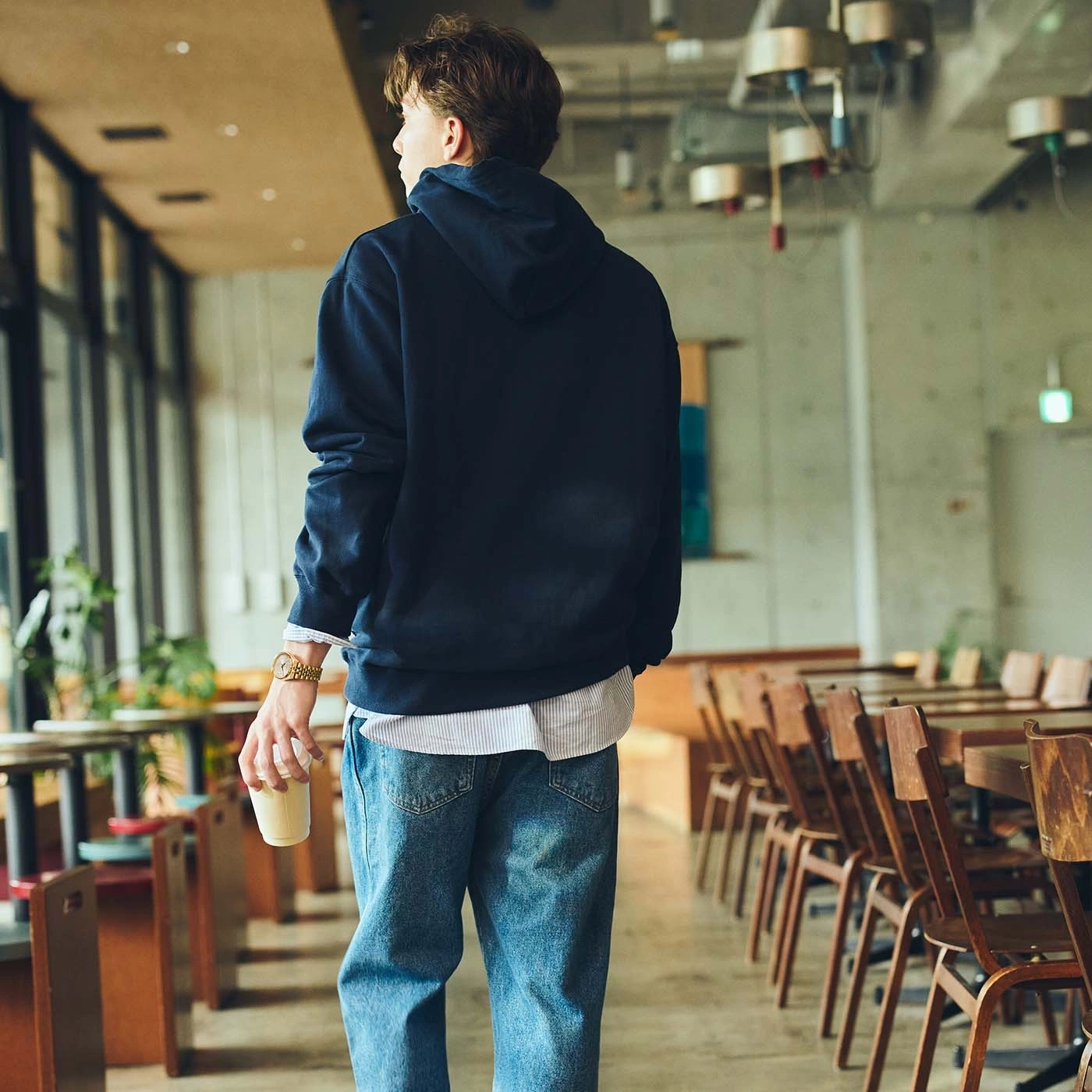 Mann im Kapuzenpullover und Jeans hält einen Kaffeebecher in einem Café