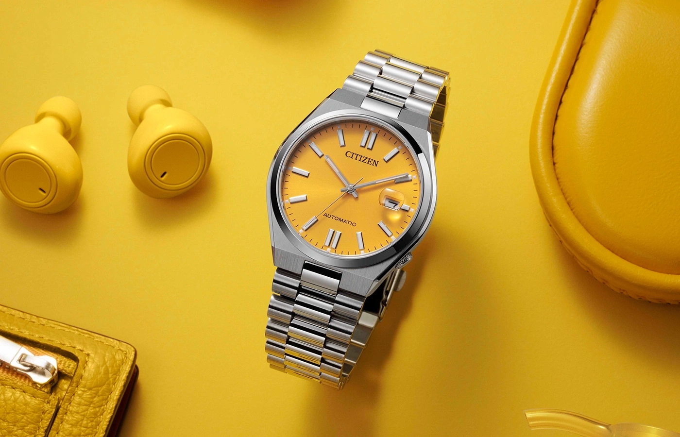 Citizen-Uhr, gelber Hintergrund, Ohrhörer, Geldbörse und eine gelbe Tasche.