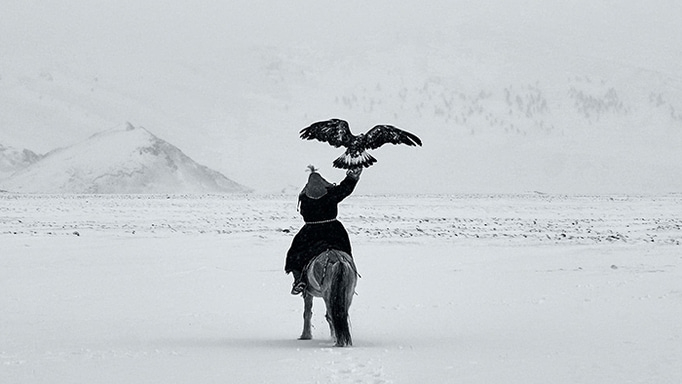 Ein Mann auf einem Pferd mit einem Adler in einer verschneiten Landschaft.