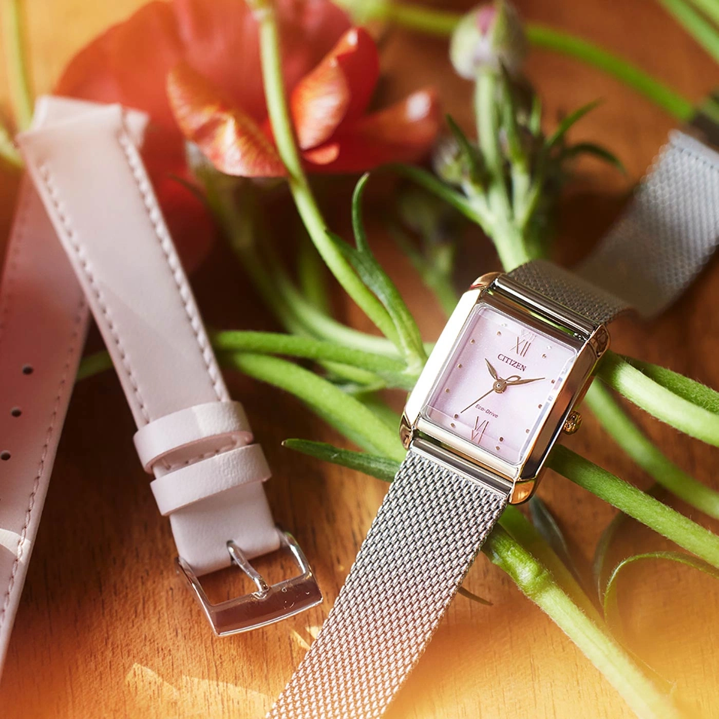 Citizen-Uhr mit rosa Zifferblatt und Mesh-Armband, mit einem Ersatz-Lederarmband und Blumen.