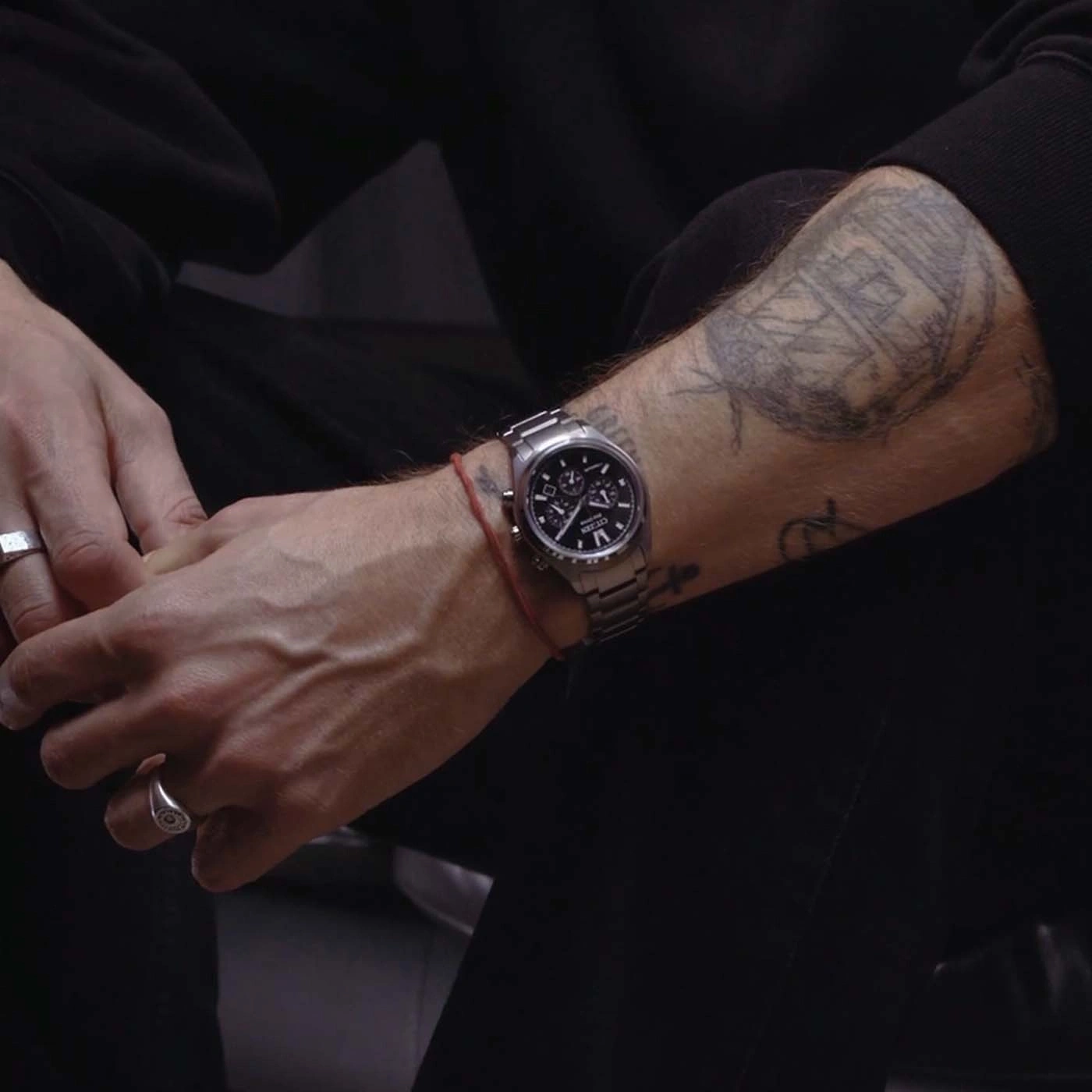 Nahaufnahme des tätowierten Arms eines Mannes mit Uhr und Ringen.