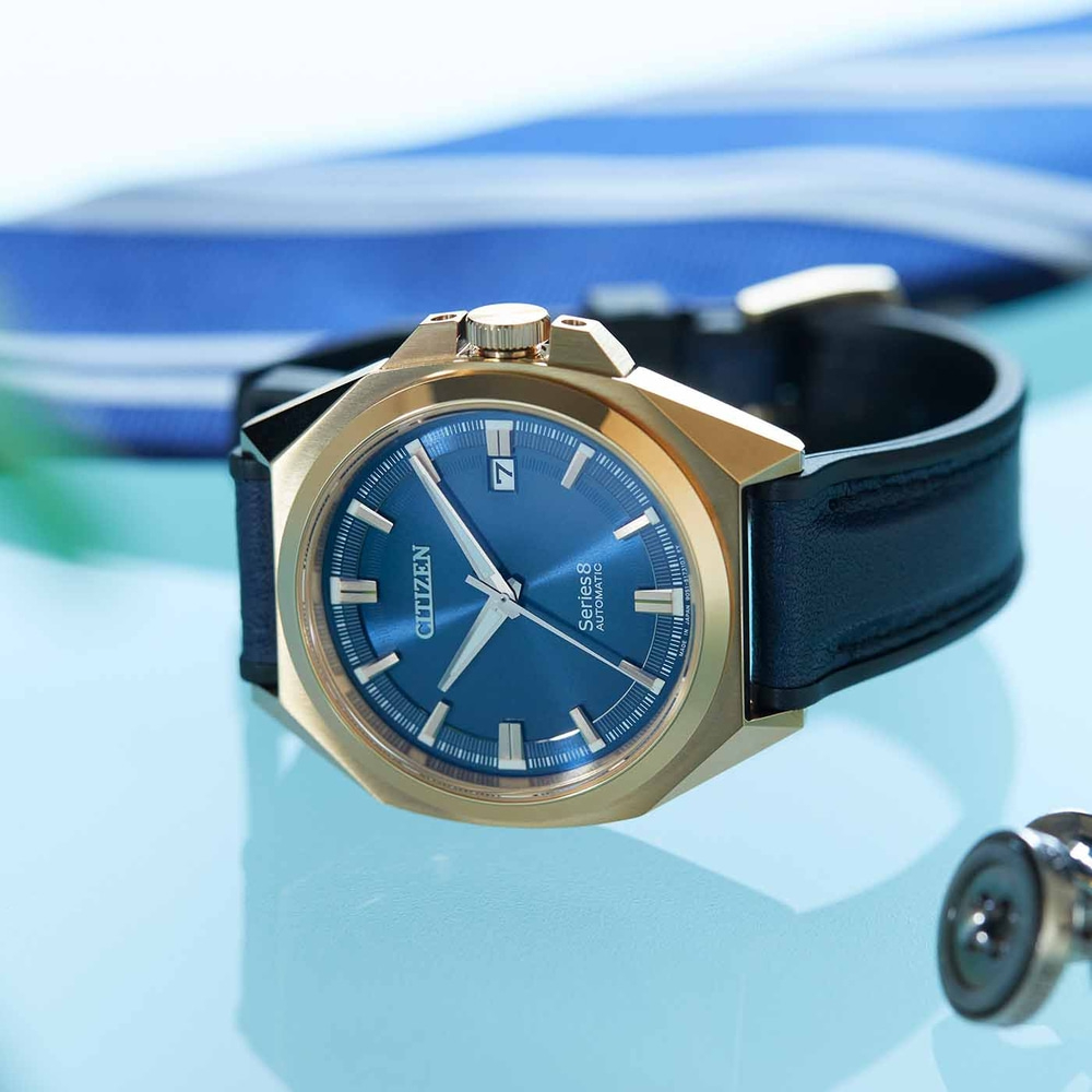 Citizen-Uhr mit blauem Zifferblatt und goldenem Gehäuse auf blauem Untergrund.