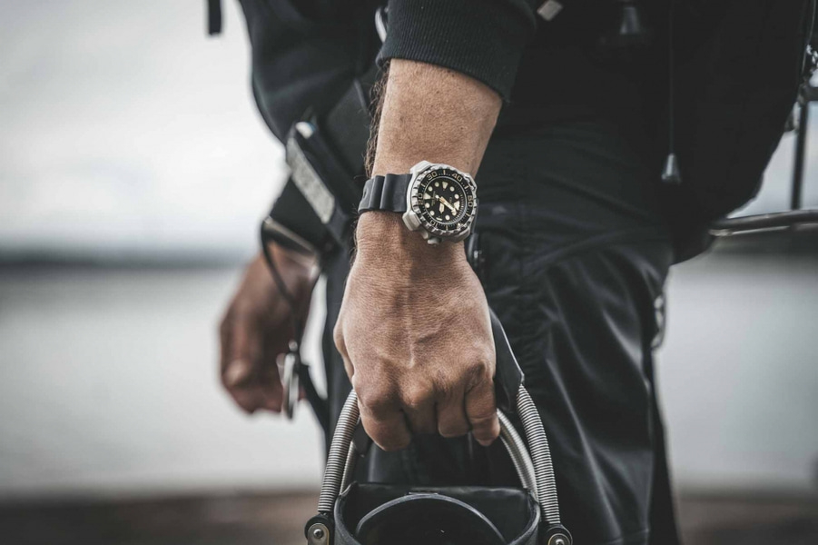 Mann mit Uhr, hält Ausrüstung, Nahaufnahme, schwarzes Outfit, im Freien