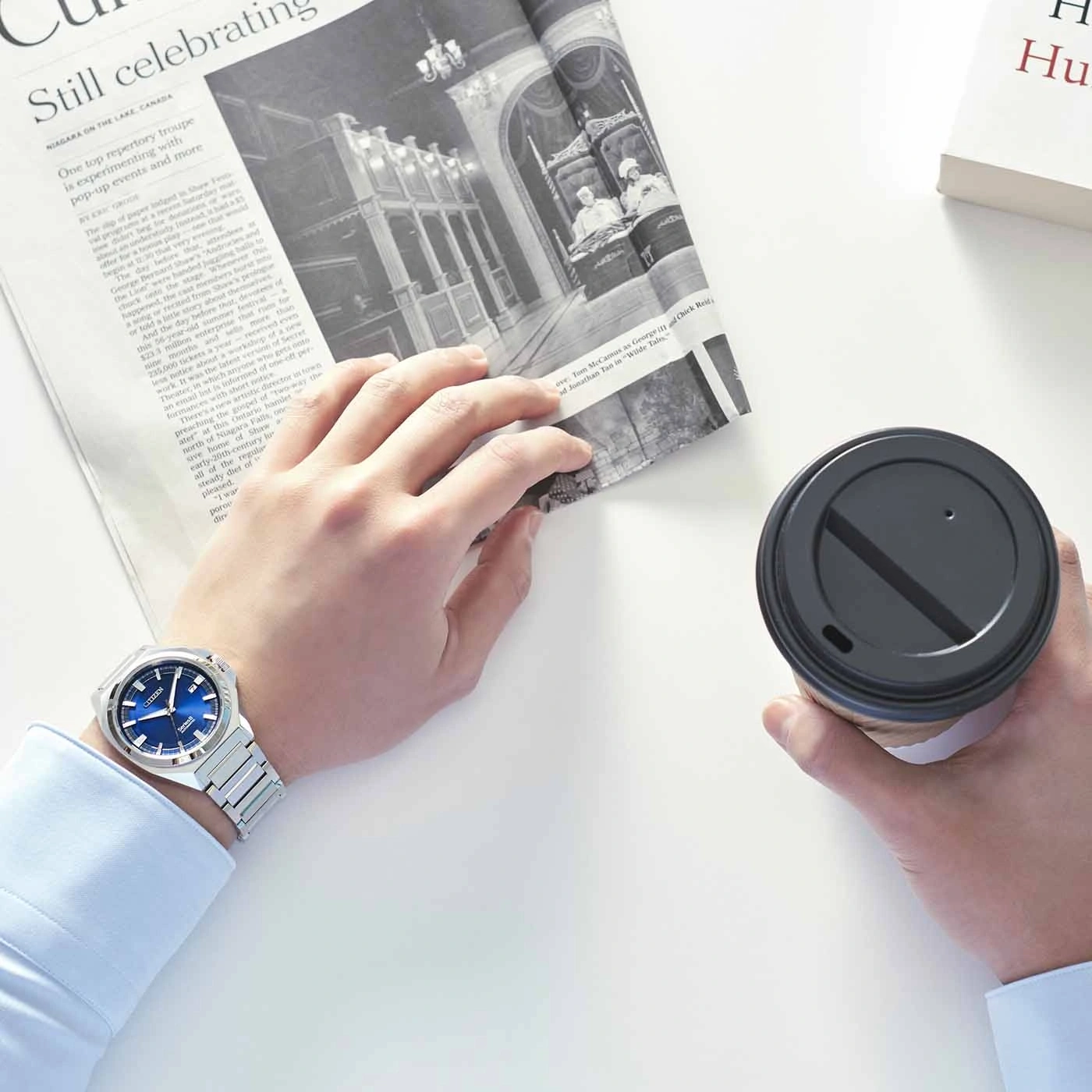 Mann hält Zeitung und Kaffee, trägt eine Uhr.