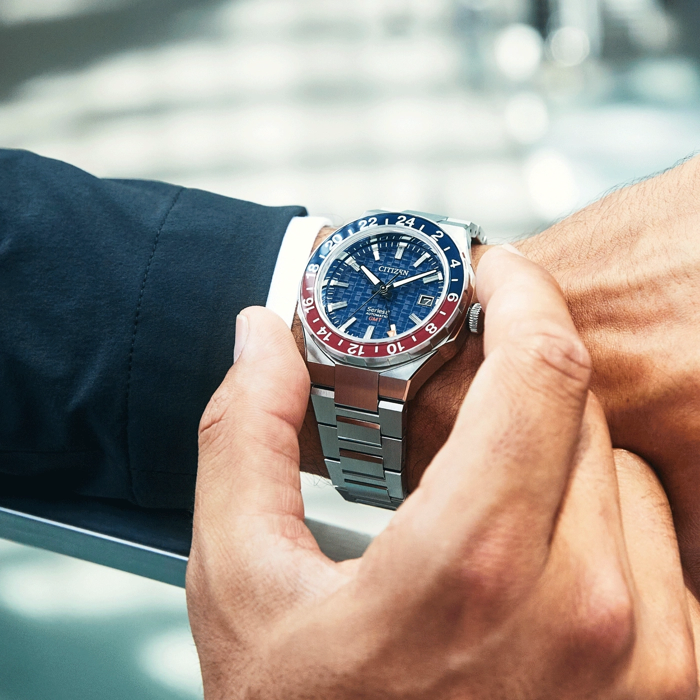 Mann trägt Citizen-Uhr. Blaue und rote Lünette. Edelstahlarmband.