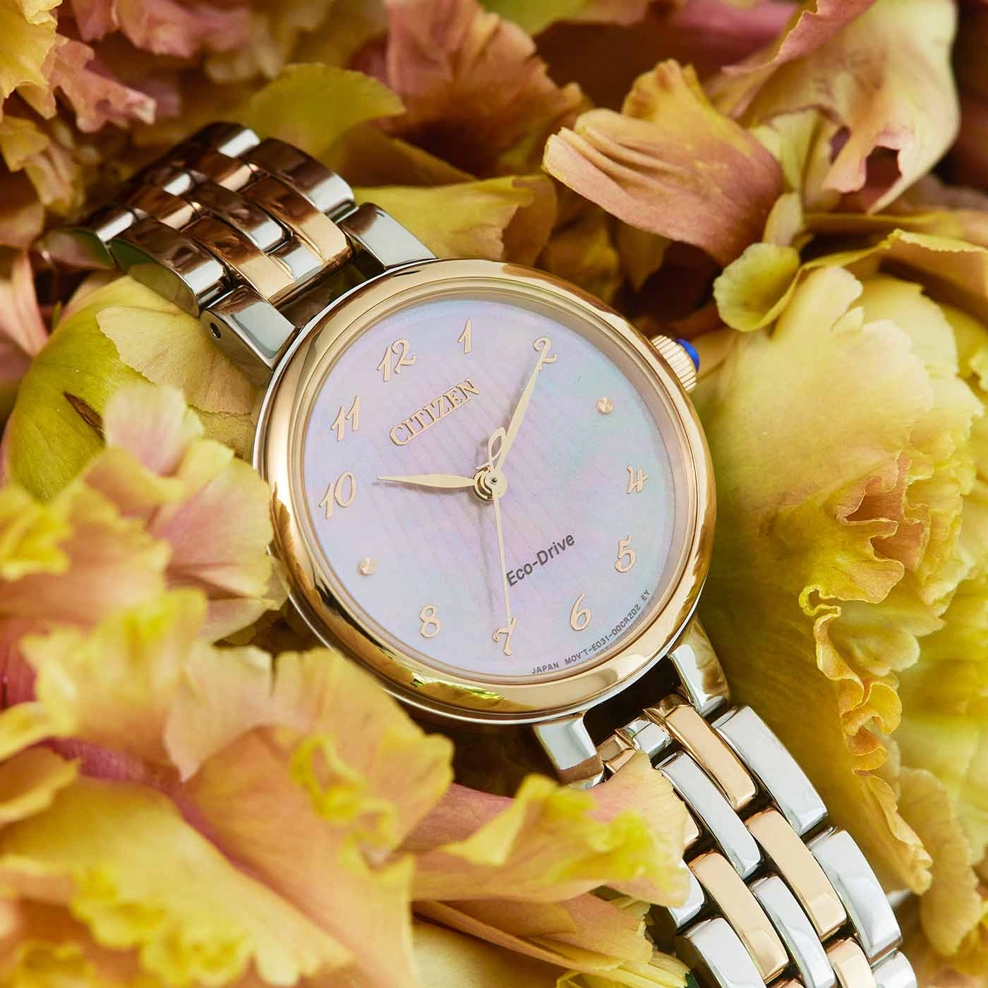 Citizen-Uhr mit Gold- und Silberband, umgeben von gelben Blumen.