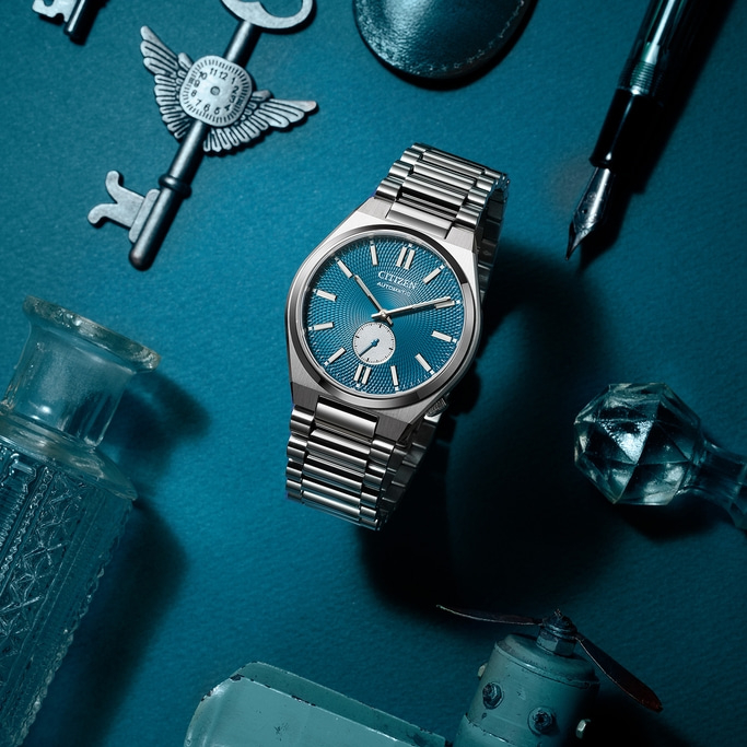 Citizen-Uhr mit blauem Zifferblatt, Schlüsseln, Stift und anderen Objekten auf blauem Untergrund.