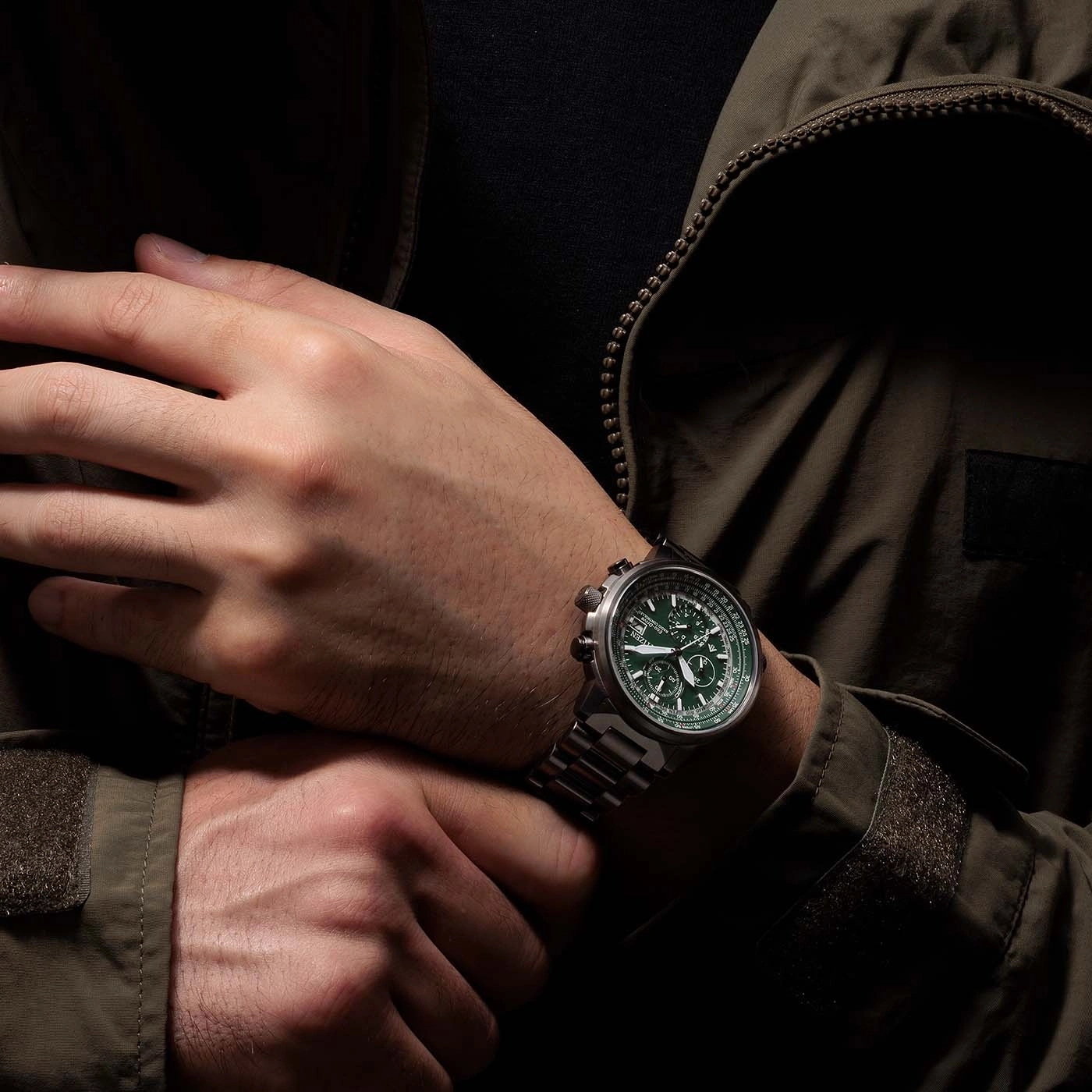 Mann mit grüner Uhr, verschränkte Hände, dunkle Jacke, Nahaufnahme