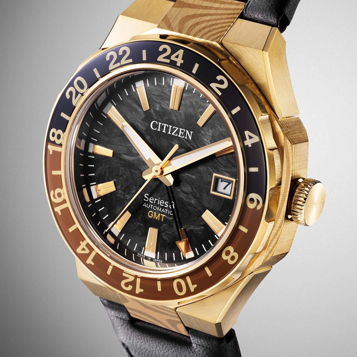 Eine Nahaufnahme einer luxuriösen goldenen Citizen GMT-Uhr mit schwarzem Zifferblatt und braunen Akzenten auf der Lünette.