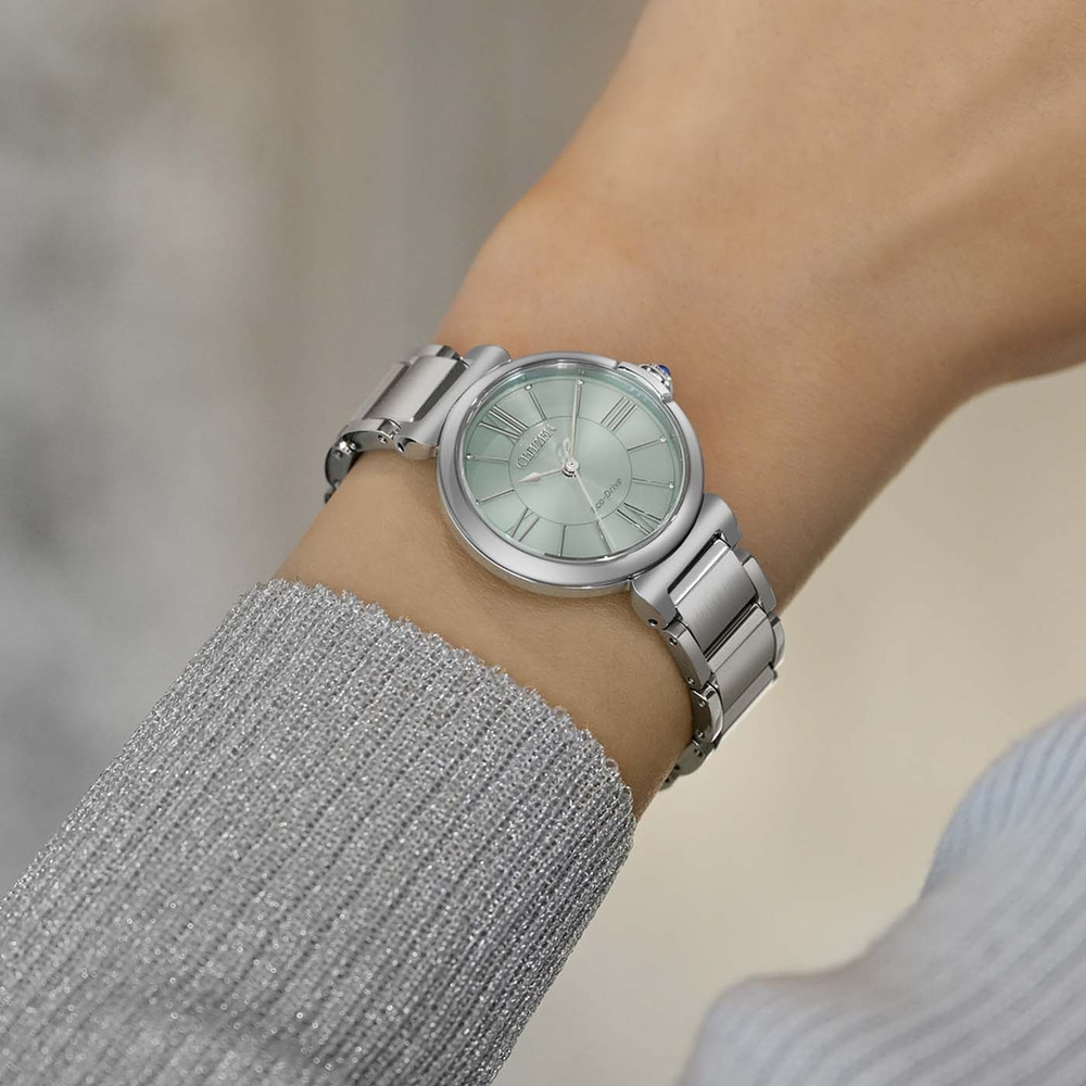 Das Handgelenk einer Frau mit einer silbernen Uhr mit hellgrünem Zifferblatt.