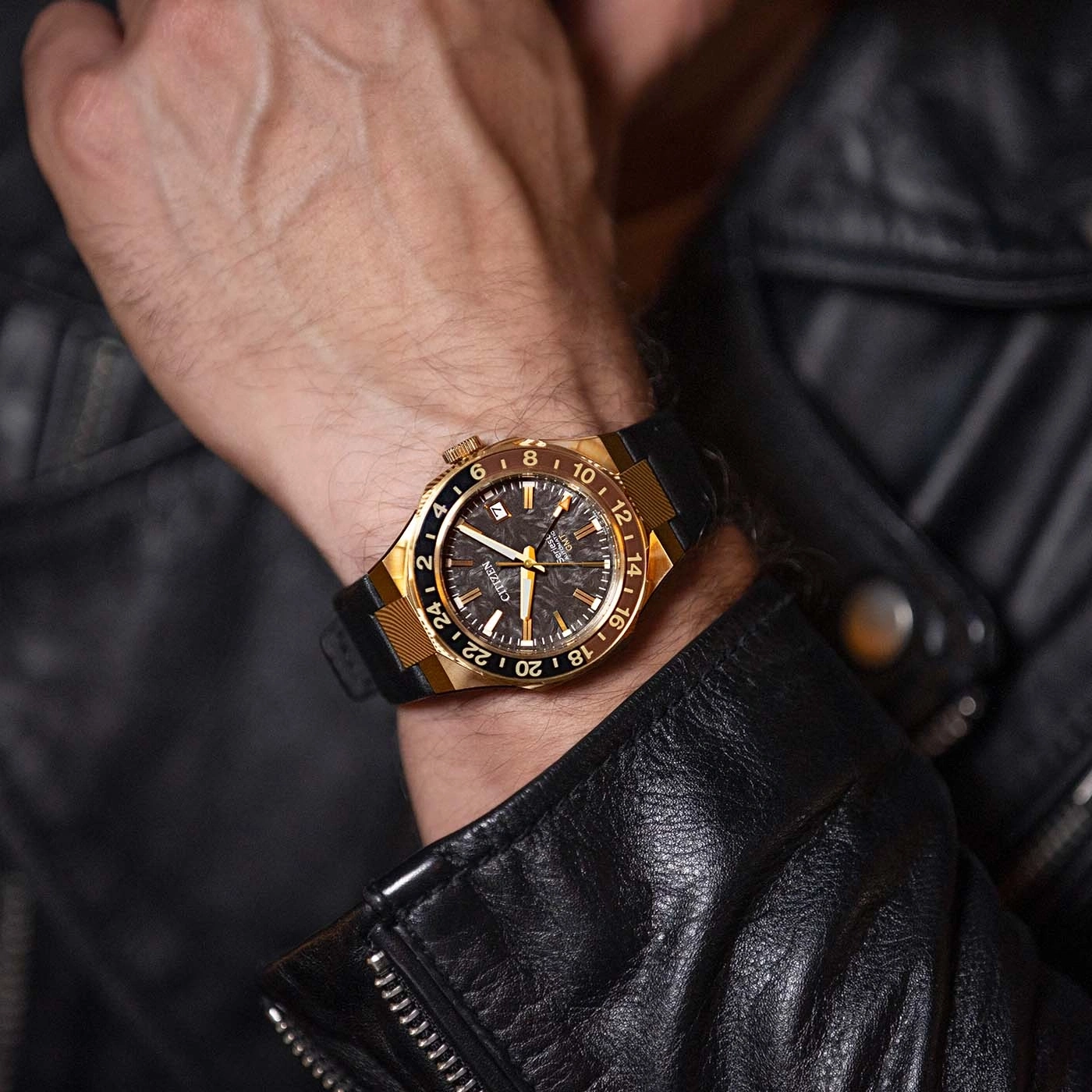 Ein Mann trägt eine gold-schwarze Citizen-Uhr am Handgelenk, bekleidet mit einer schwarzen Lederjacke.