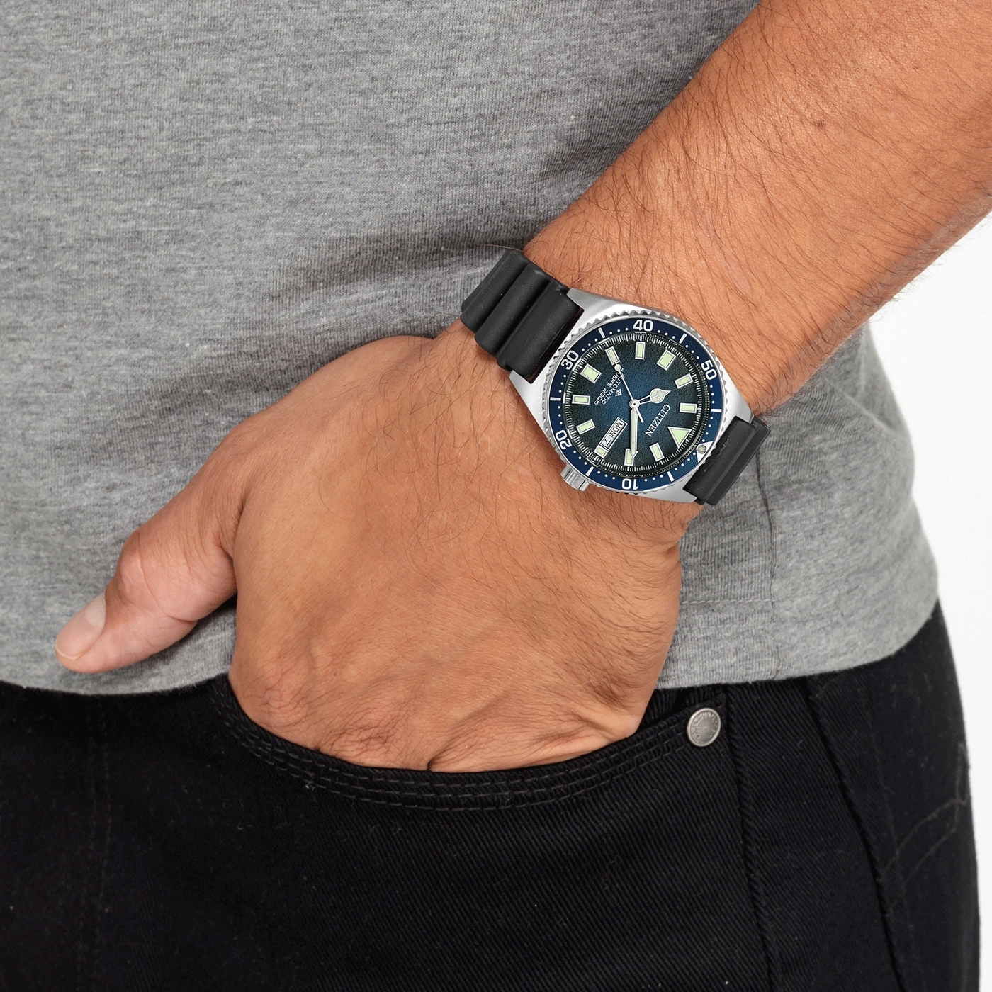 Mann mit Citizen-Uhr, Hand in der Tasche, graues Hemd, schwarze Jeans.