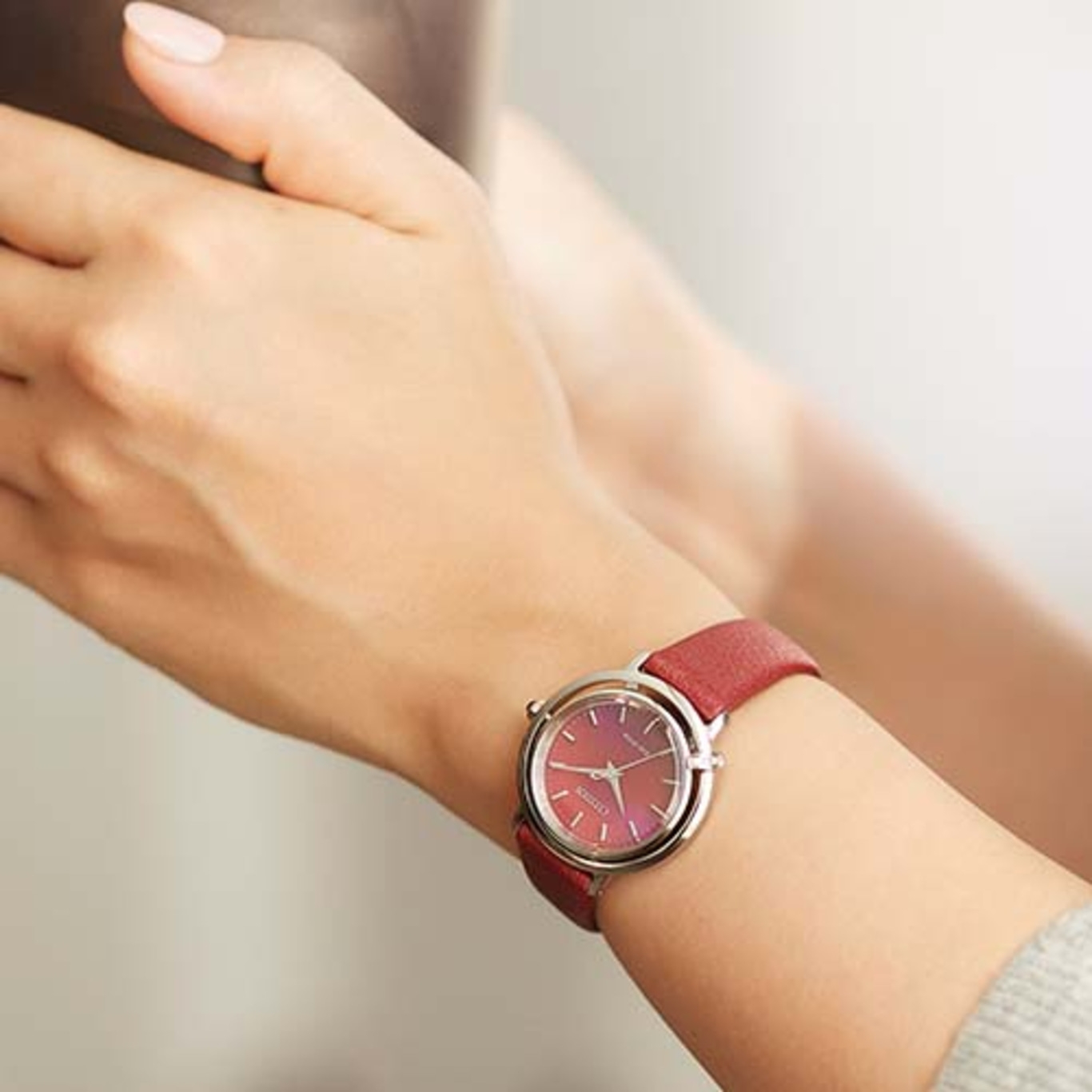 Ein rotes Armbanduhr an einem Handgelenk. Die Uhr hat ein rotes Armband und ein silbernes Gehäuse.