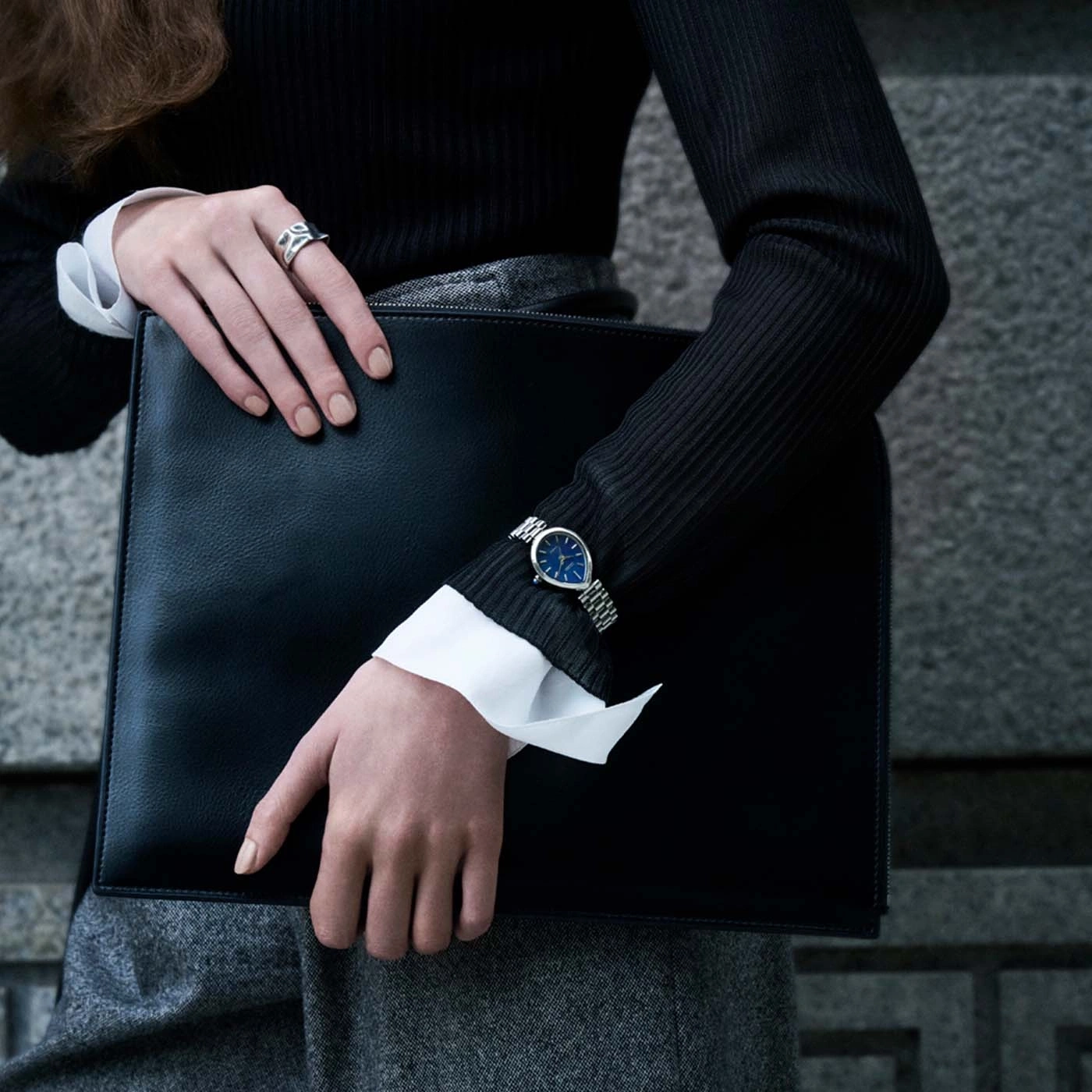 Frau hält schwarze Aktentasche, trägt Uhr und Ring.