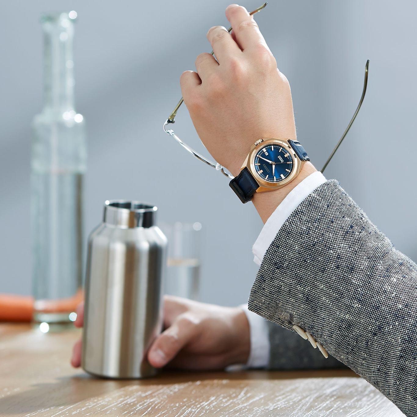 Mann mit Uhr, Brille, Wasserflasche am Tisch. Geschäftsmann im Anzug.