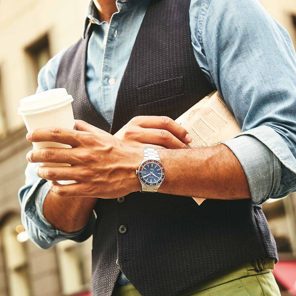 Mann mit Kaffee und Zeitung, trägt Uhr und Weste, im Freien.