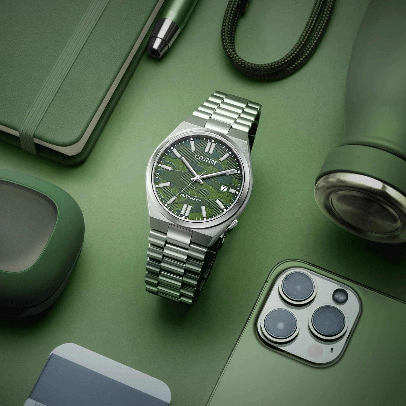 Grüne Uhr, Telefon, Notizbuch, Stift und Wasserflasche auf grünem Hintergrund.
