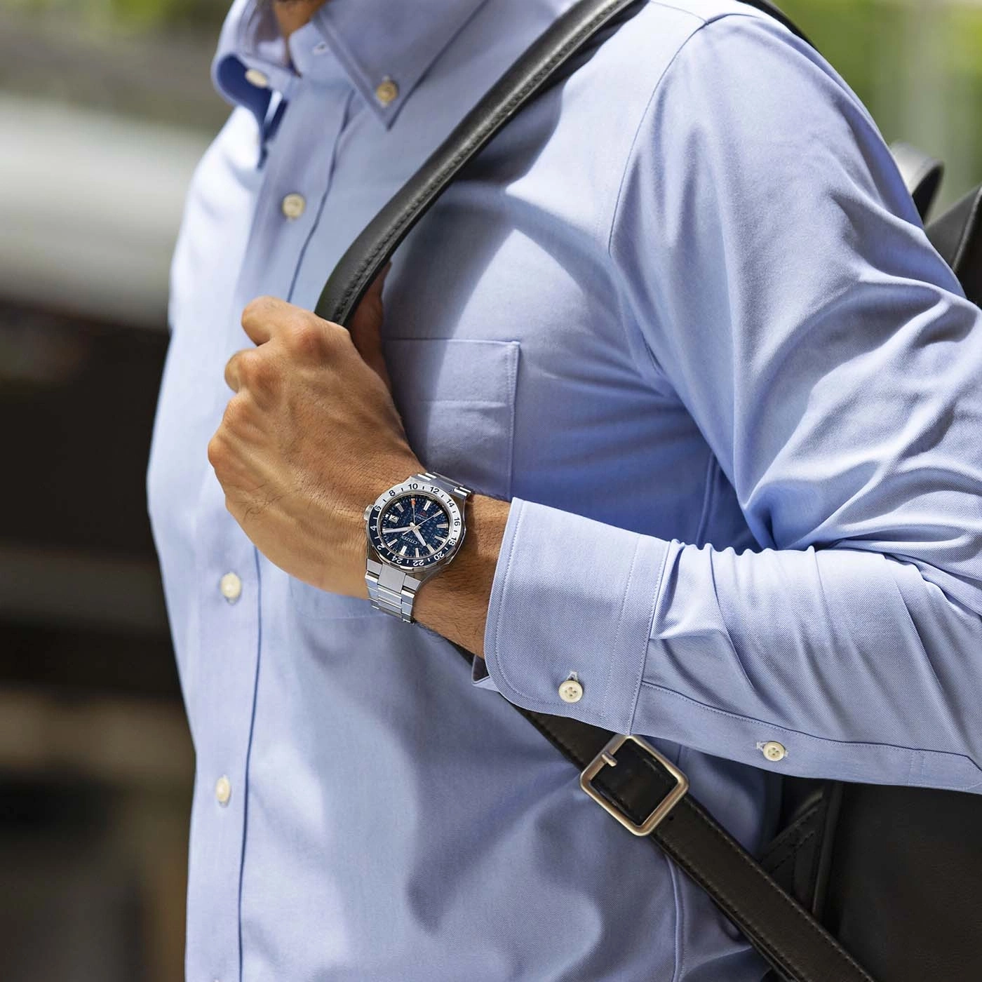 Mann mit Uhr und blauem Hemd mit schwarzer Tasche auf der Schulter.