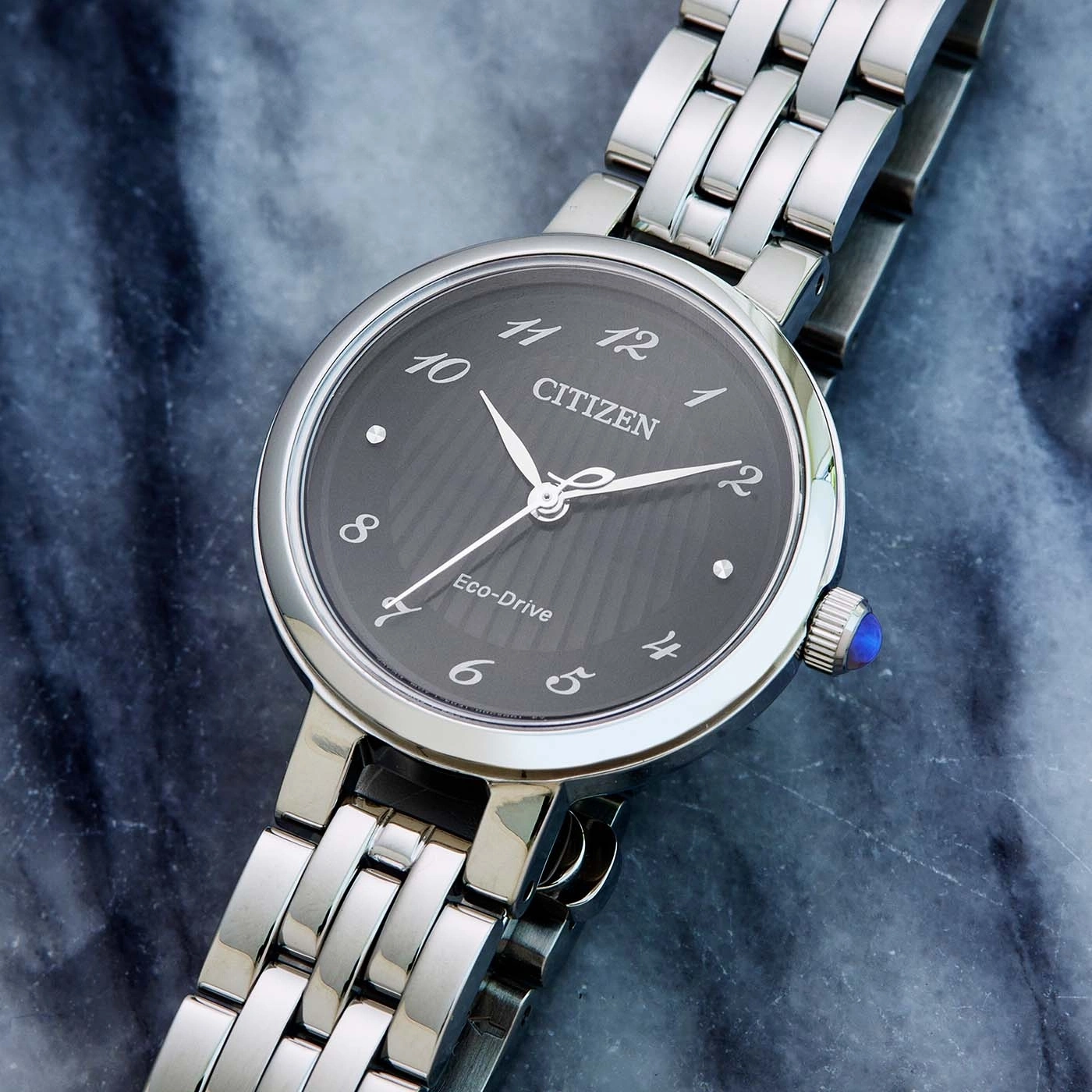 Citizen-Uhr mit dunklem Zifferblatt und silbernem Armband auf Marmoroberfläche.