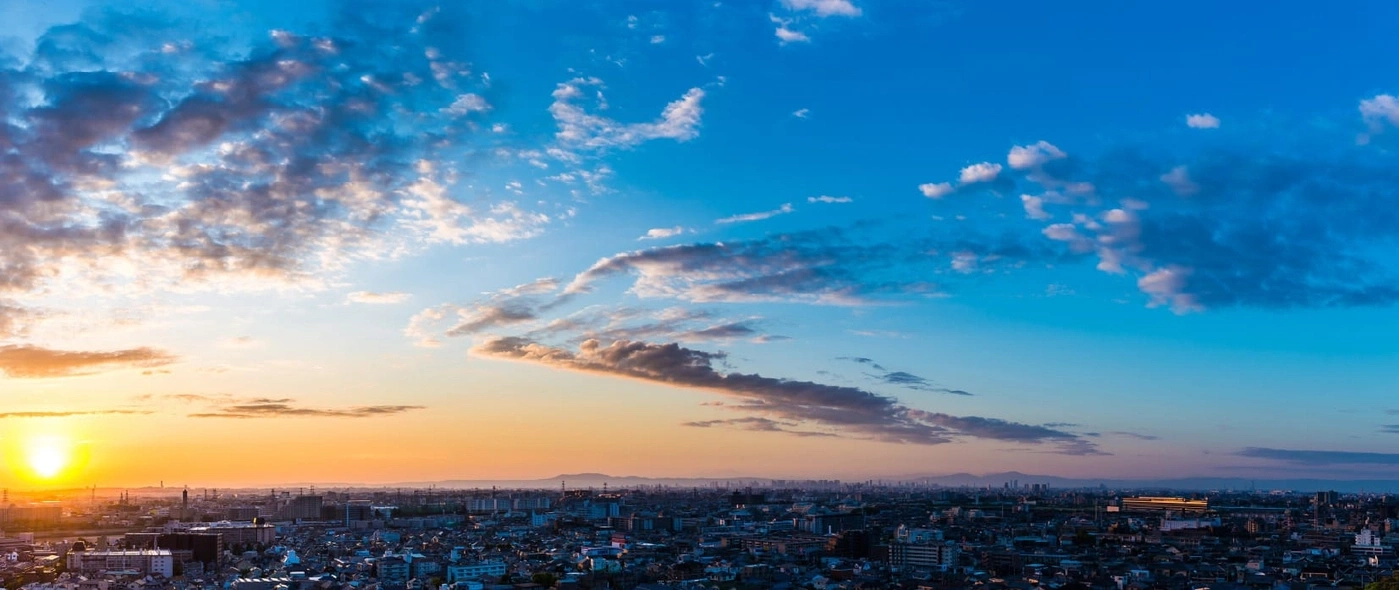 Stadtlandschaft bei Sonnenuntergang mit lebhaftem Himmel und verstreuten Wolken über Gebäuden.